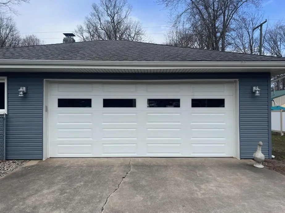 A white long panel garage door fitted to a navy sided house