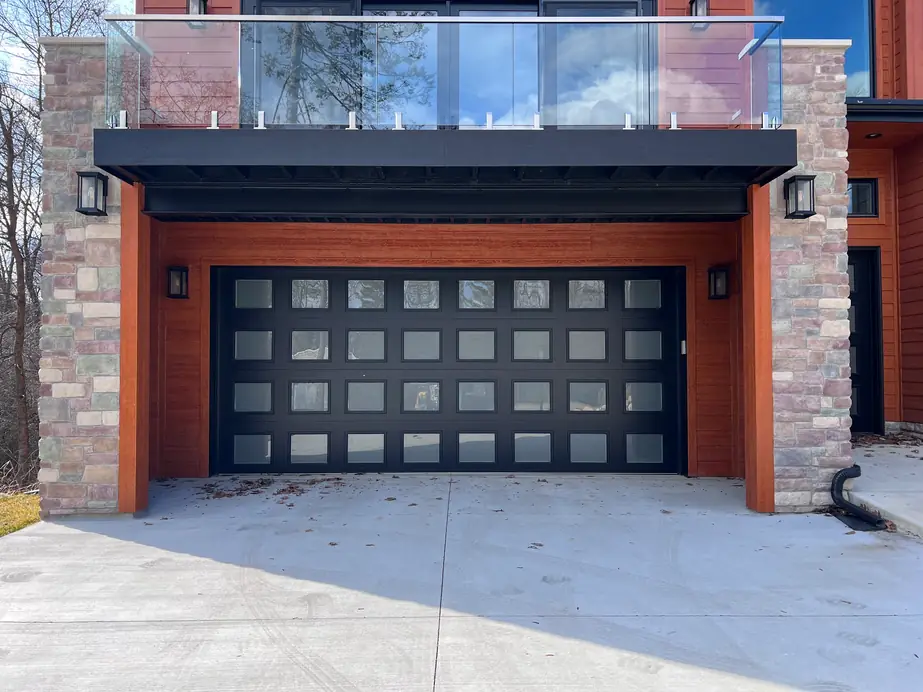 A modern black full view garage door on a contemporary stone and wood house